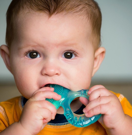 A baby boy holding a solid teether in his mouth to help with the teething process