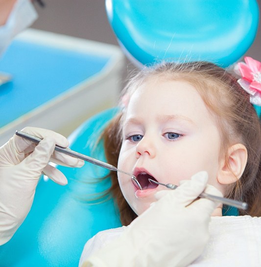 A dental hygienist examining a little girl’s smile before administering fluoride treatment