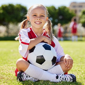Child sits on grass with soccer ball