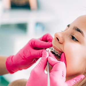 Gloved hands adjusting patient’s braces