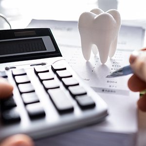 Closeup of hands with pen and calculator at desk next to model tooth