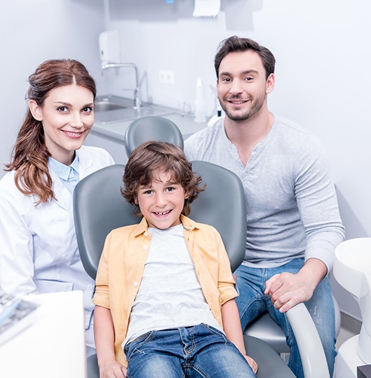 Little boy smiling at dentist alongside dad