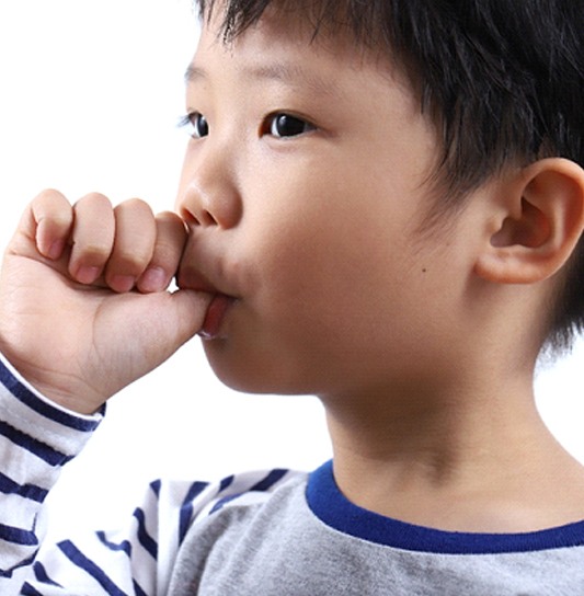 A little boy wearing a white and blue striped shirt sucks his thumb