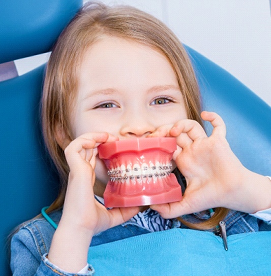 A young girl holds a mouth mold with braces in front of her actual mouth