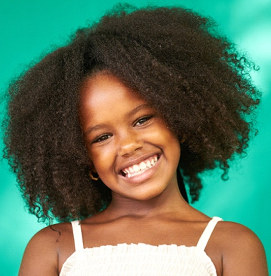 A young girl wearing a white dress smiles wide after receiving silver diamine fluoride treatment