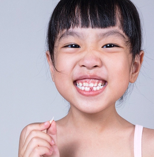 A little girl holds a tooth that has been extracted from her mouth