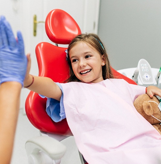 Child giving kid's dentist a high five in treatment chair
