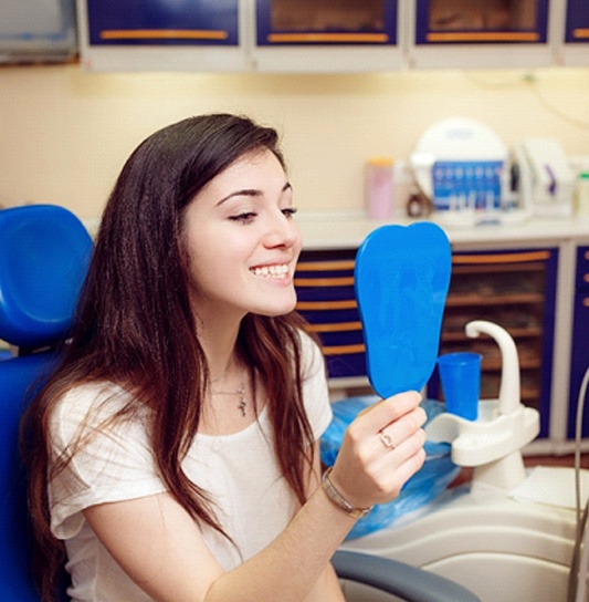 A young girl looks at her smile in the mirror while at the dentist’s office after receiving dental sealants