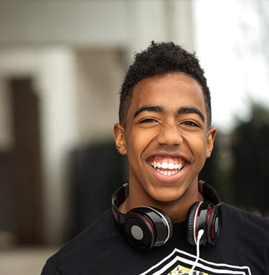 A young male teen wearing headphones around his neck and smiling after receiving fluoride treatment during an appointment with his dentist