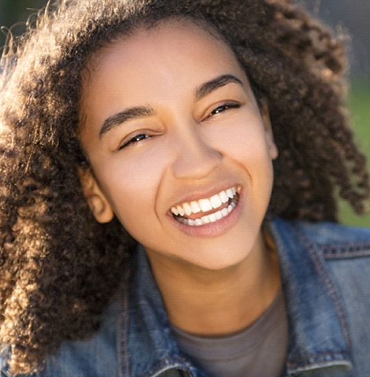 A young girl wearing a denim shirt and smiling after having a tooth-colored filling placed