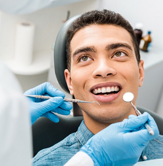 A male teen smiles while a dentist checks his teeth and gums for problem areas