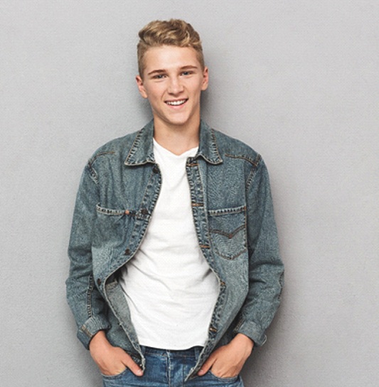 A male teen stands with his hands in his pockets and smiles after receiving a customized dental crown