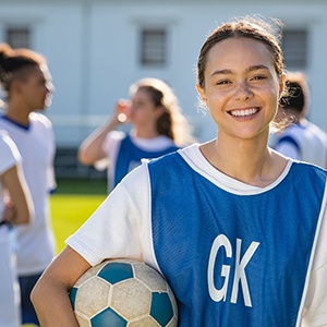 Smiling teen holding soccer ball on field