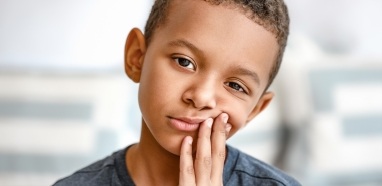 Young boy in need of emergency dentistry holding jaw