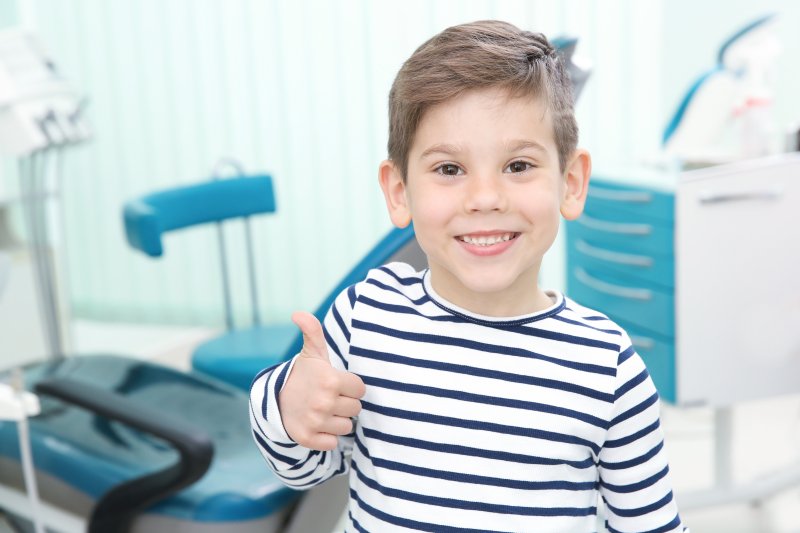 a little boy wearing a striped shirt and giving a thumbs-up signal after seeing his pediatric dentist in Cumming, GA