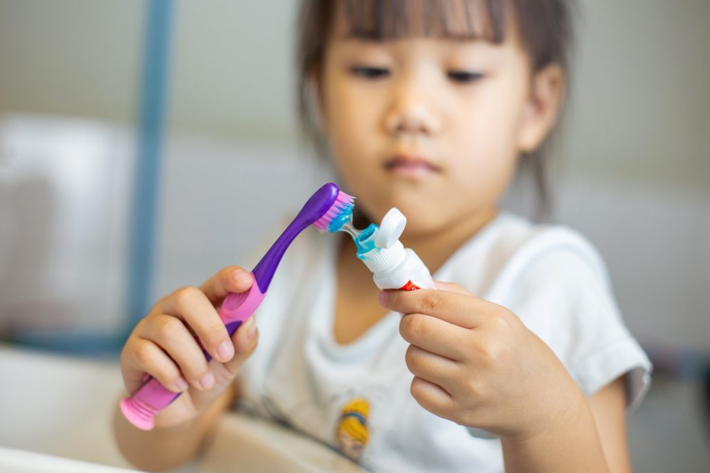 Young girl putting toothpaste on toothbrush