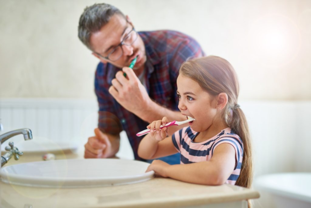 Dad and daughter brushing their teeth together in bathroom