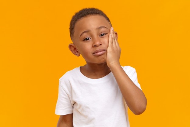 child experiencing dental emergency holding cheek