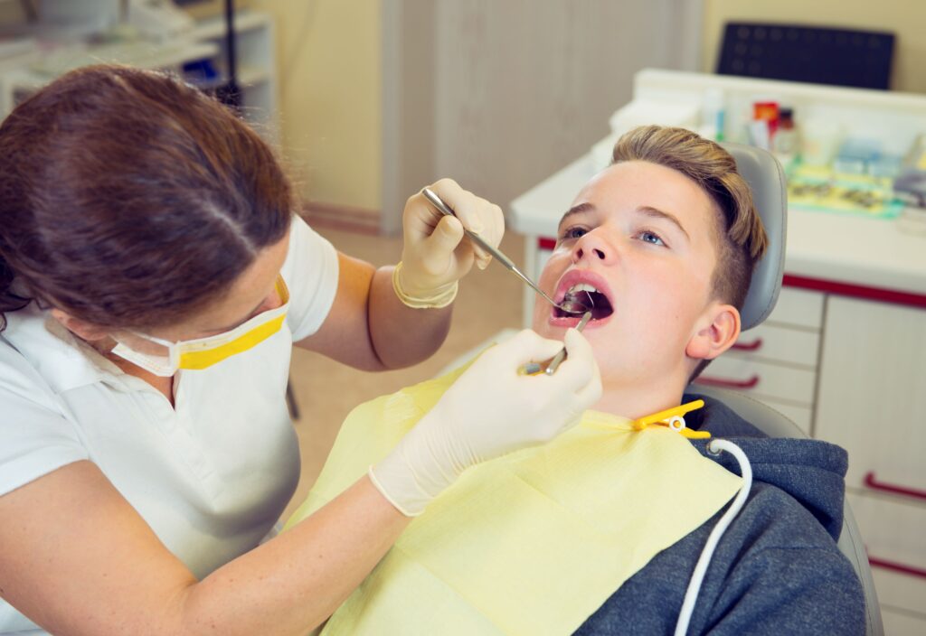 Dentist in yellow gloves examining teenager's mouth